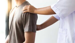 Adult receiving a gentle back assessment while standing beside a spine model in a bright clinic room.