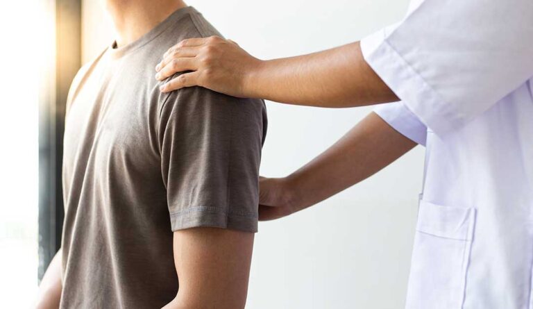 Adult receiving a gentle back assessment while standing beside a spine model in a bright clinic room.